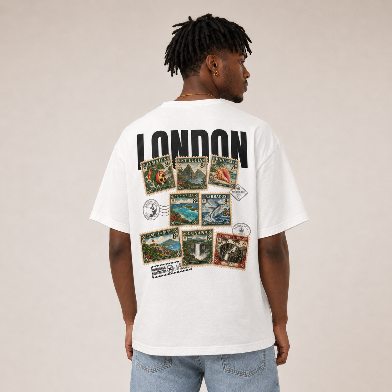 A man with shoulder-length locs seen from behind wearing the white Maknesan tee, the black LONDON wordmark and the Caribbean stamp collage at their highest contrast.